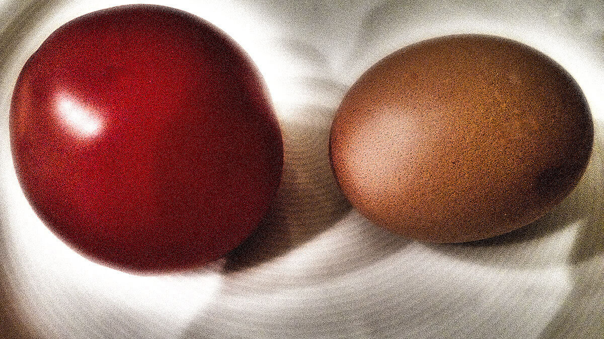 Ein rotes und ein ungefärbtes, braunes Ei auf einem Teller
